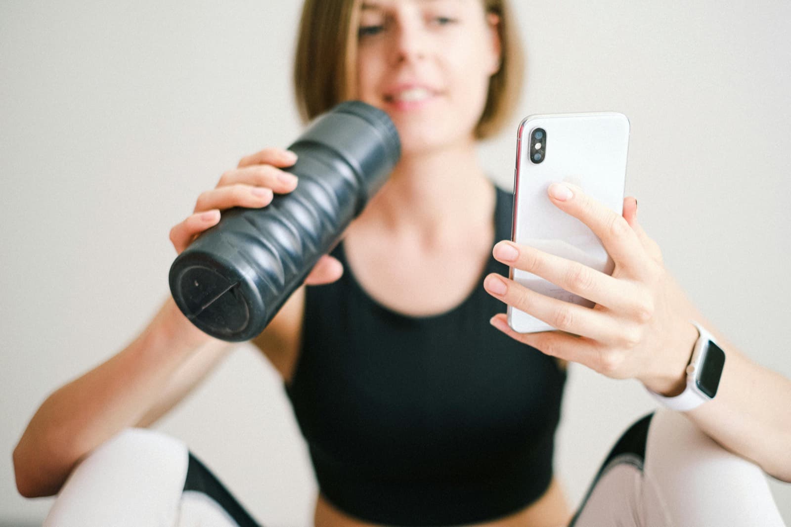 Woman resting after a workout, holding a water bottle and checking her phone