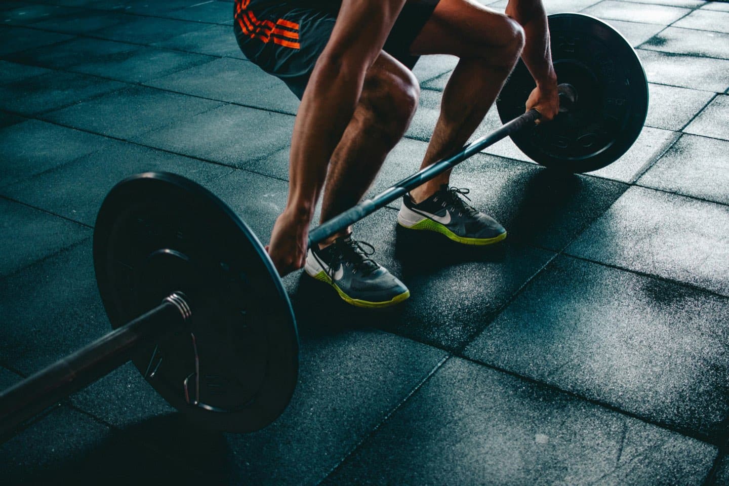 Athlete gripping a loaded barbell for a deadlift in a dark gym